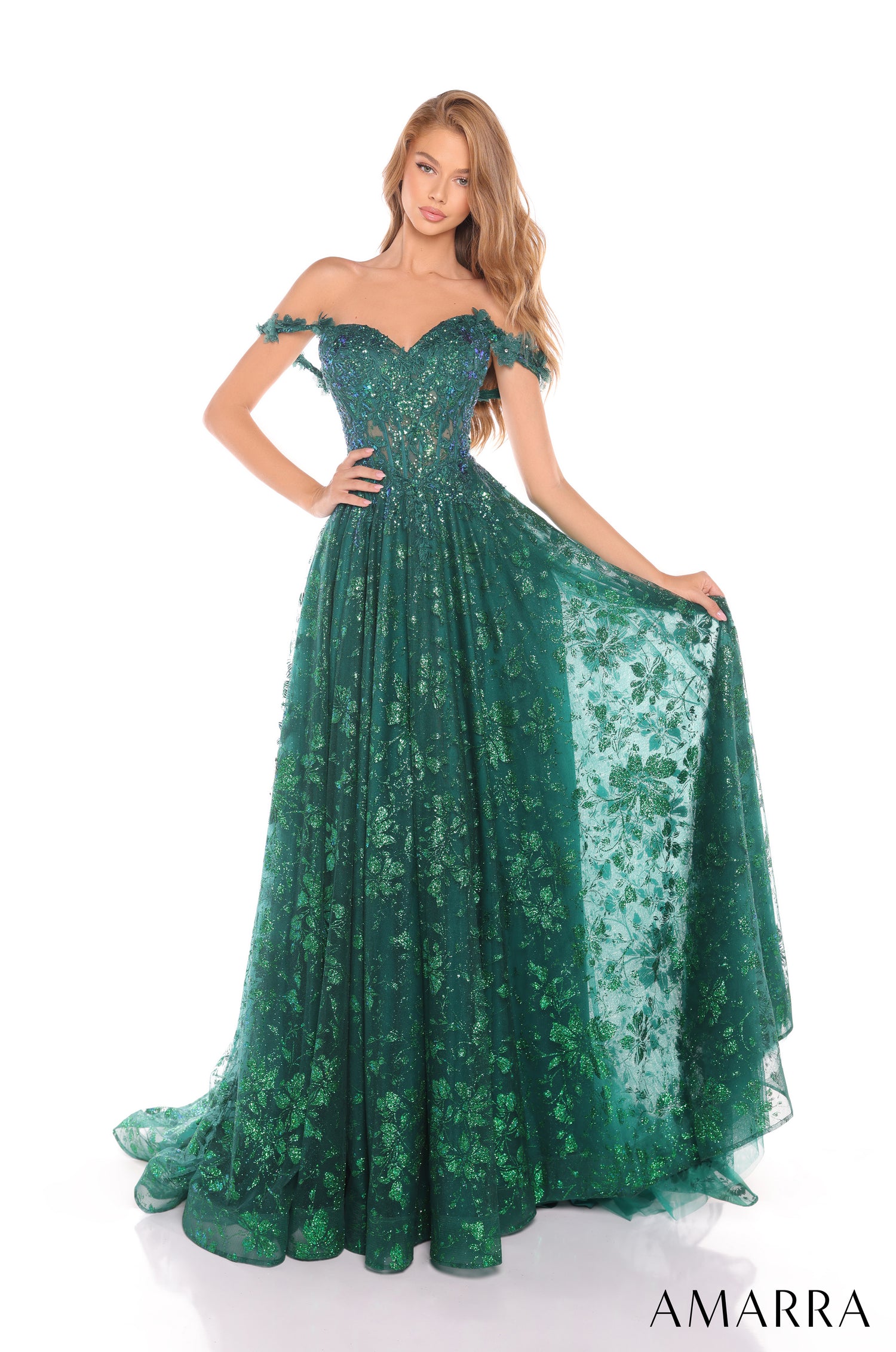 A model wears a sparkling emerald off-shoulder ball gown with floral lace and a sweeping full skirt.