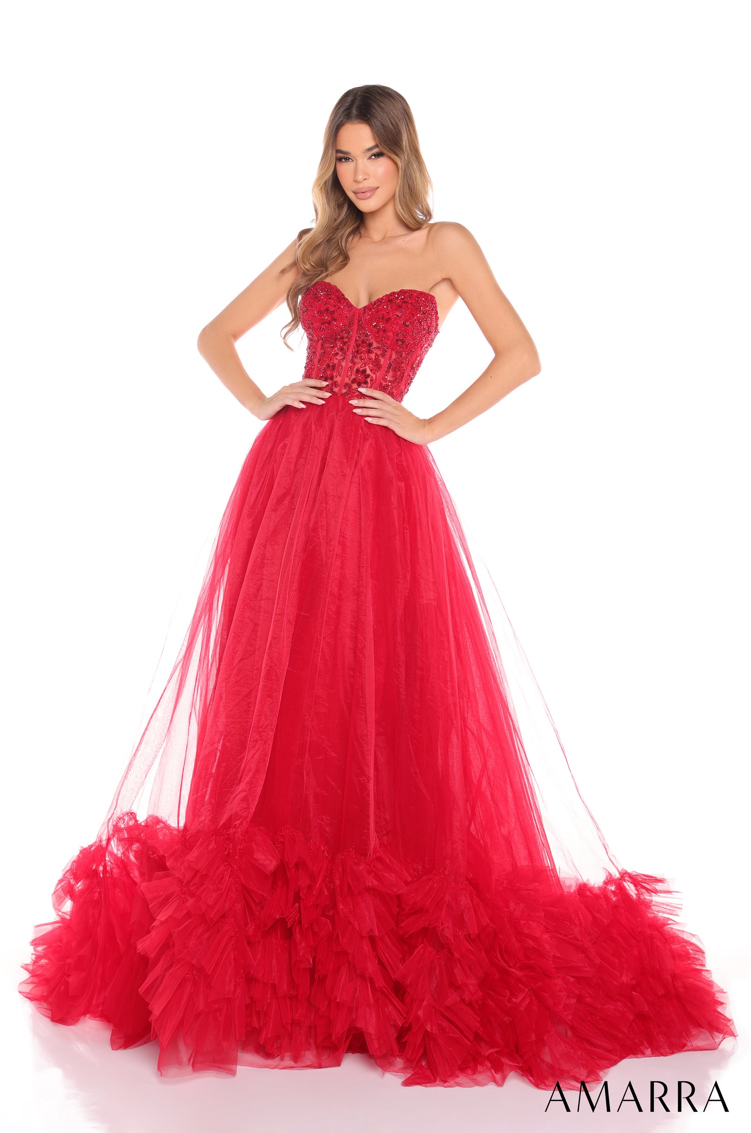 A woman wears a red strapless ball gown with a beaded corset top and voluminous tulle skirt by Amarra.