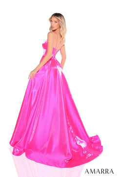 A model wears a floor-length, hot pink satin ball gown with a corset-style bodice and a dramatic train.