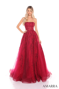 A woman models a wine-colored strapless ball gown with intricate lace detailing and a full tulle skirt.