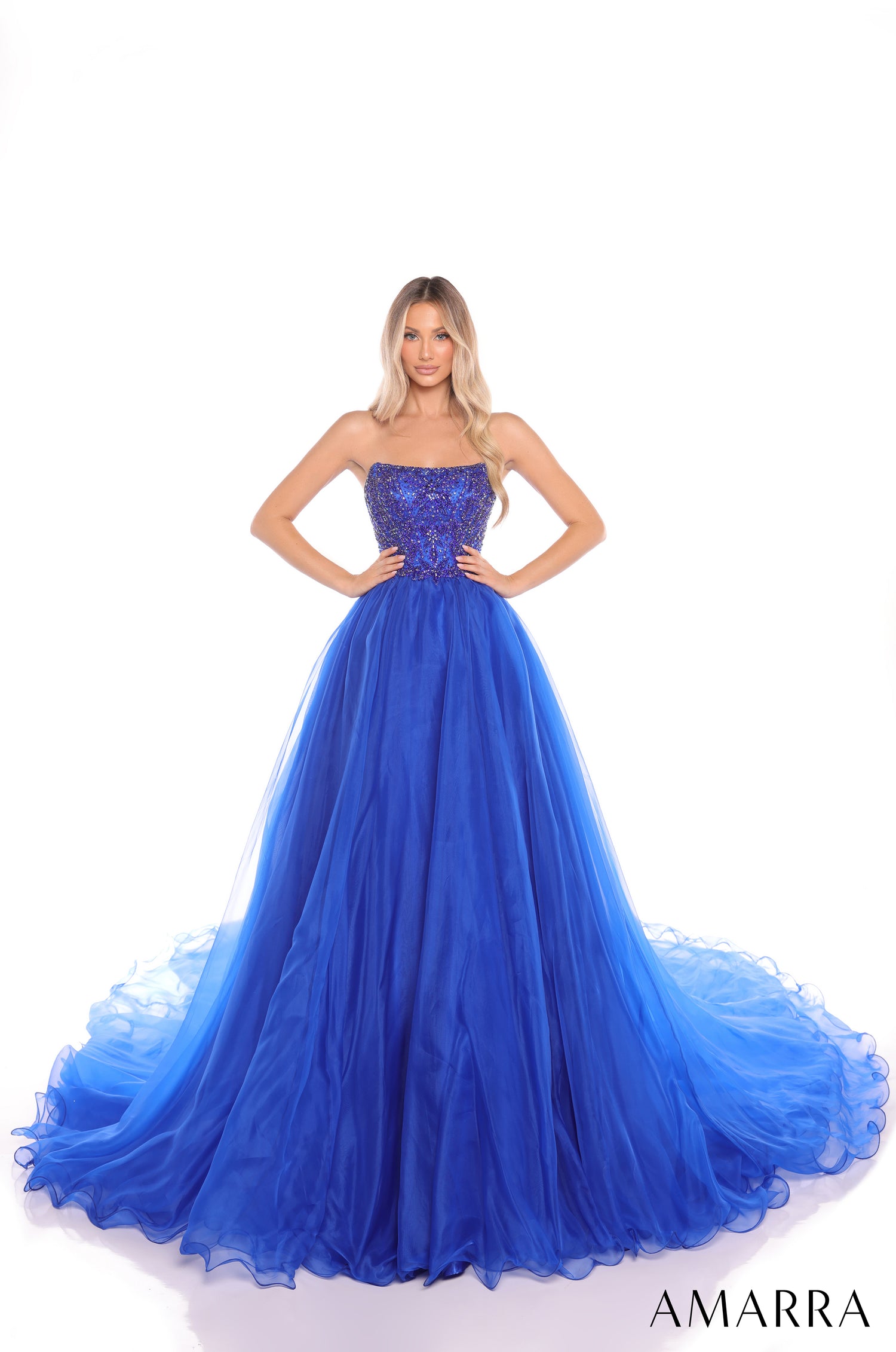 A model wears a strapless, sequined Royal Blue ball gown with a full, flowing tulle skirt.