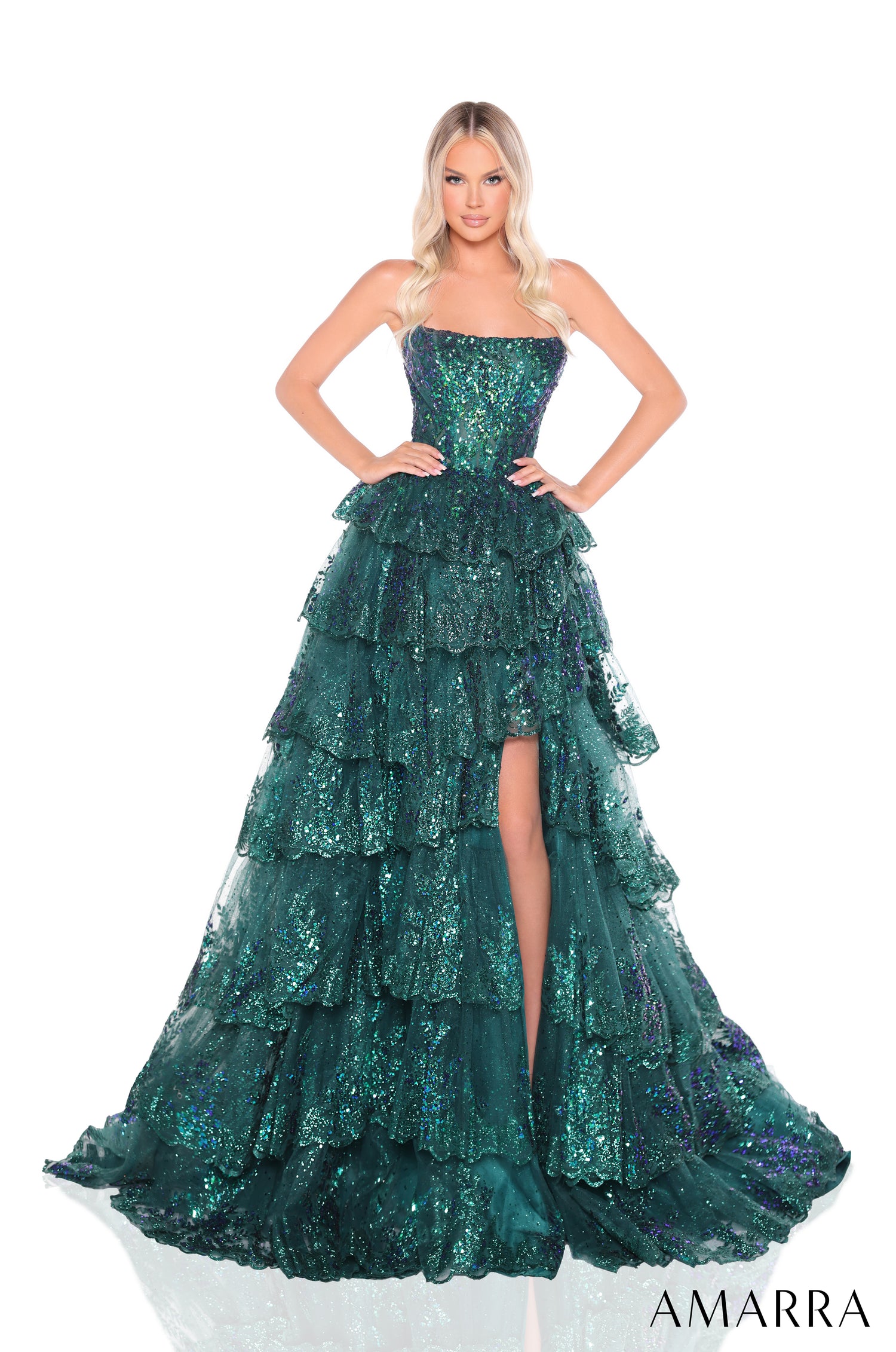 A blonde model wears a strapless, tiered emerald sequin ball gown with a high leg slit by Amarra.