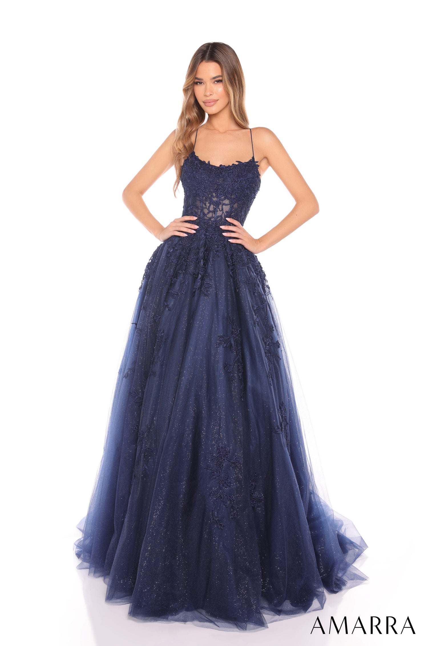 A model wears a navy blue ball gown with spaghetti straps, lace details, and a full tulle skirt.