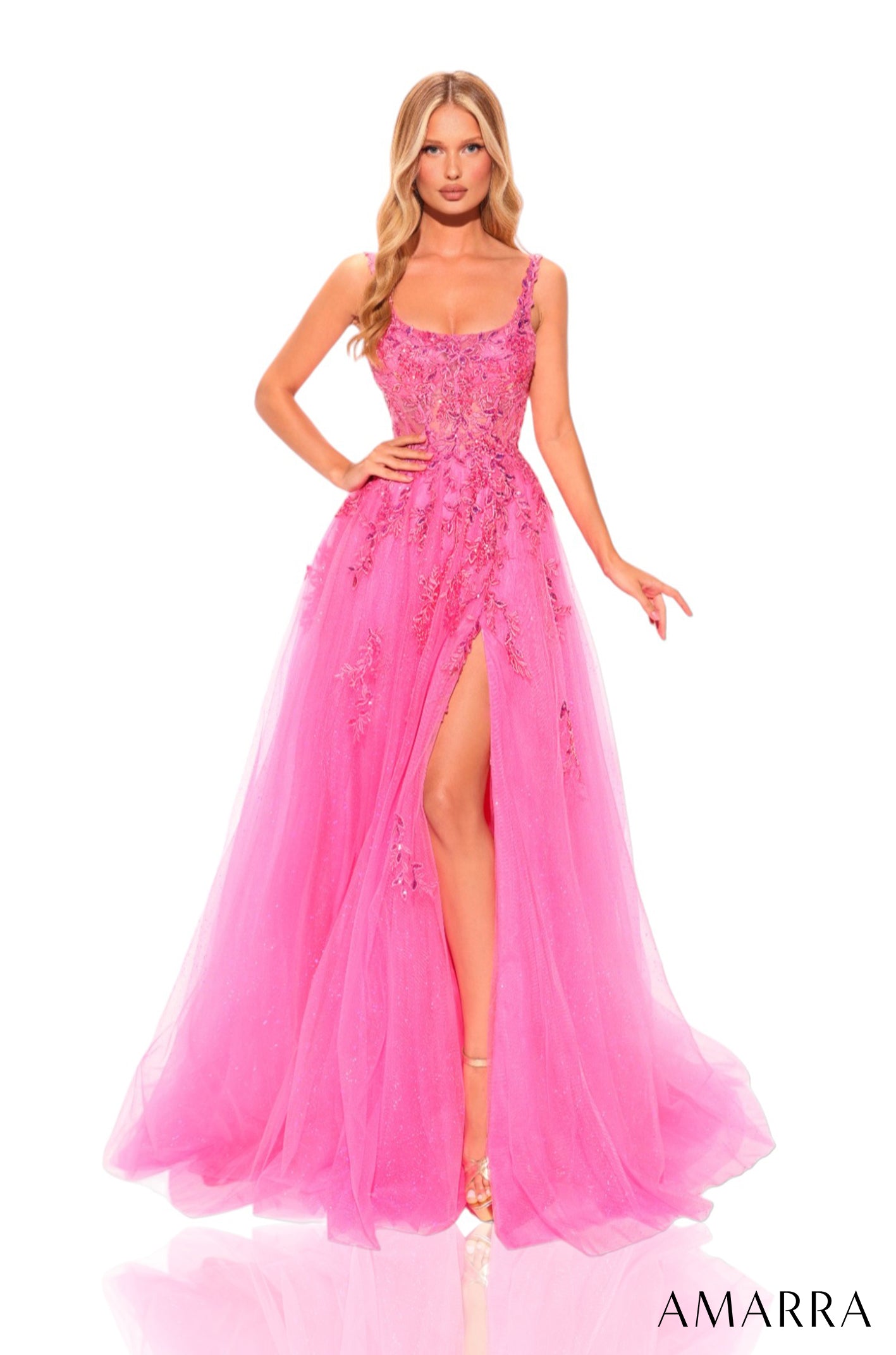 A model wears a floor-length fuchsia tulle gown with floral appliqués and a high side slit.