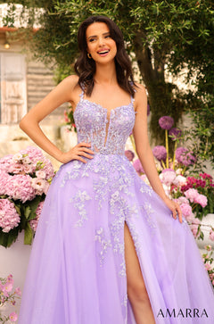 A woman in a lavender ball gown with floral embellishments smiles in a garden of pink and purple flowers.