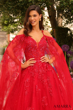 A smiling model wears a vibrant red ballgown with elaborate floral lace and sheer cape sleeves.