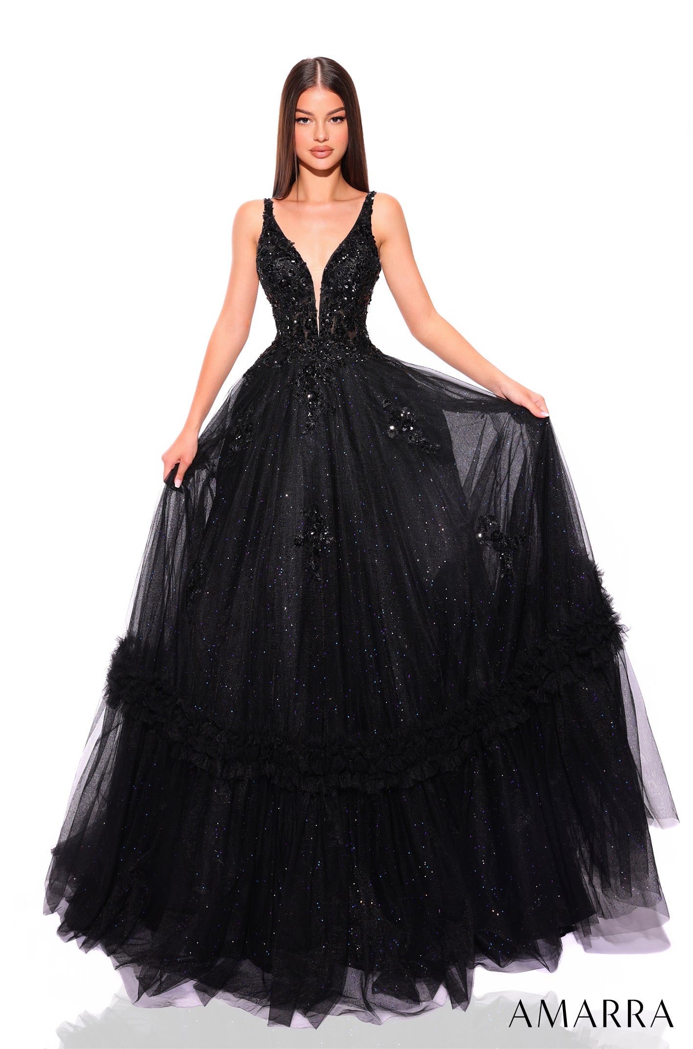 A woman wears a Black sparkling tulle ball gown with a plunging neckline and feathered skirt details.