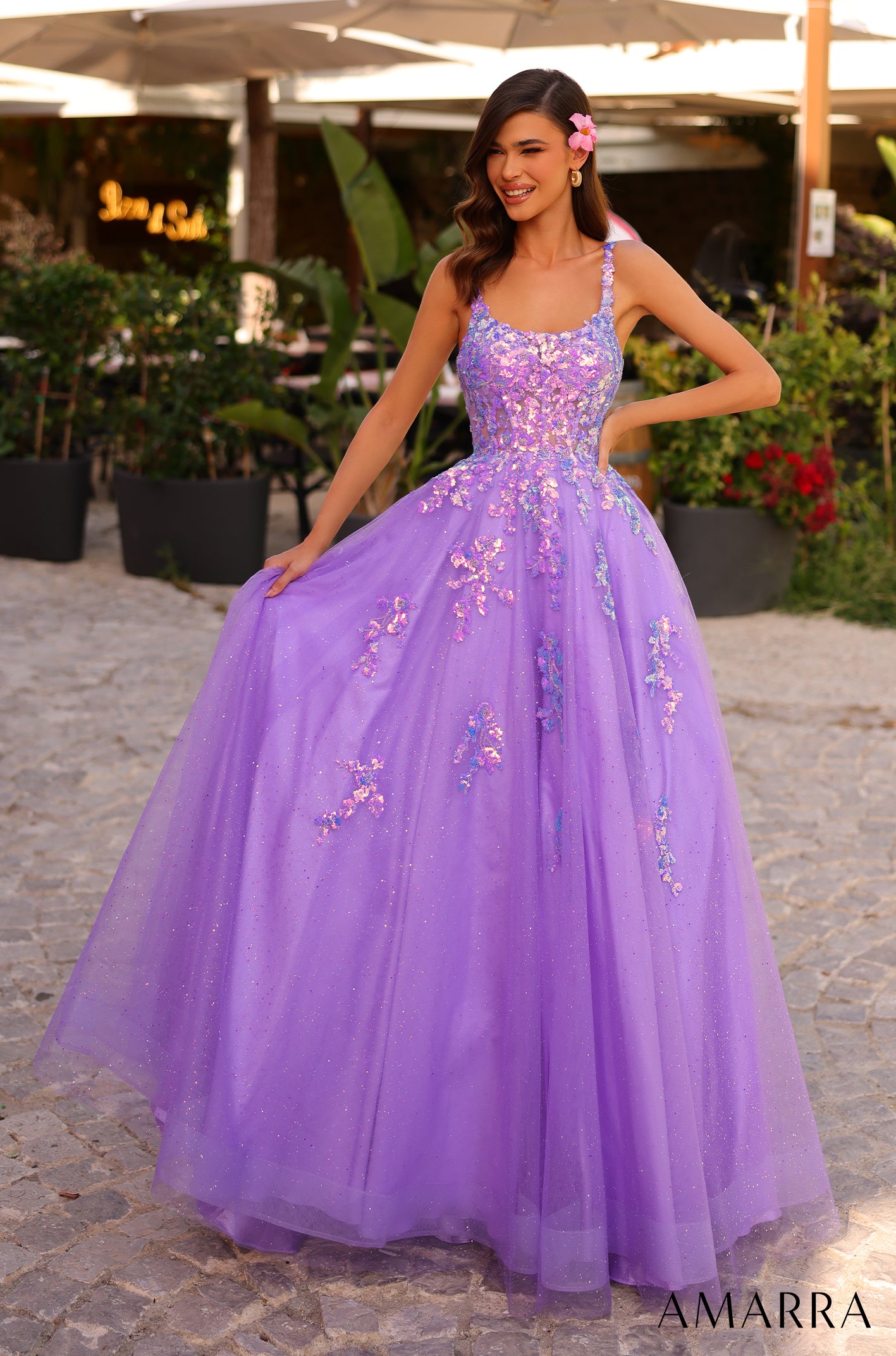 A woman wears a sparkling dark lilac ball gown with floral embellishments, standing in a garden setting.