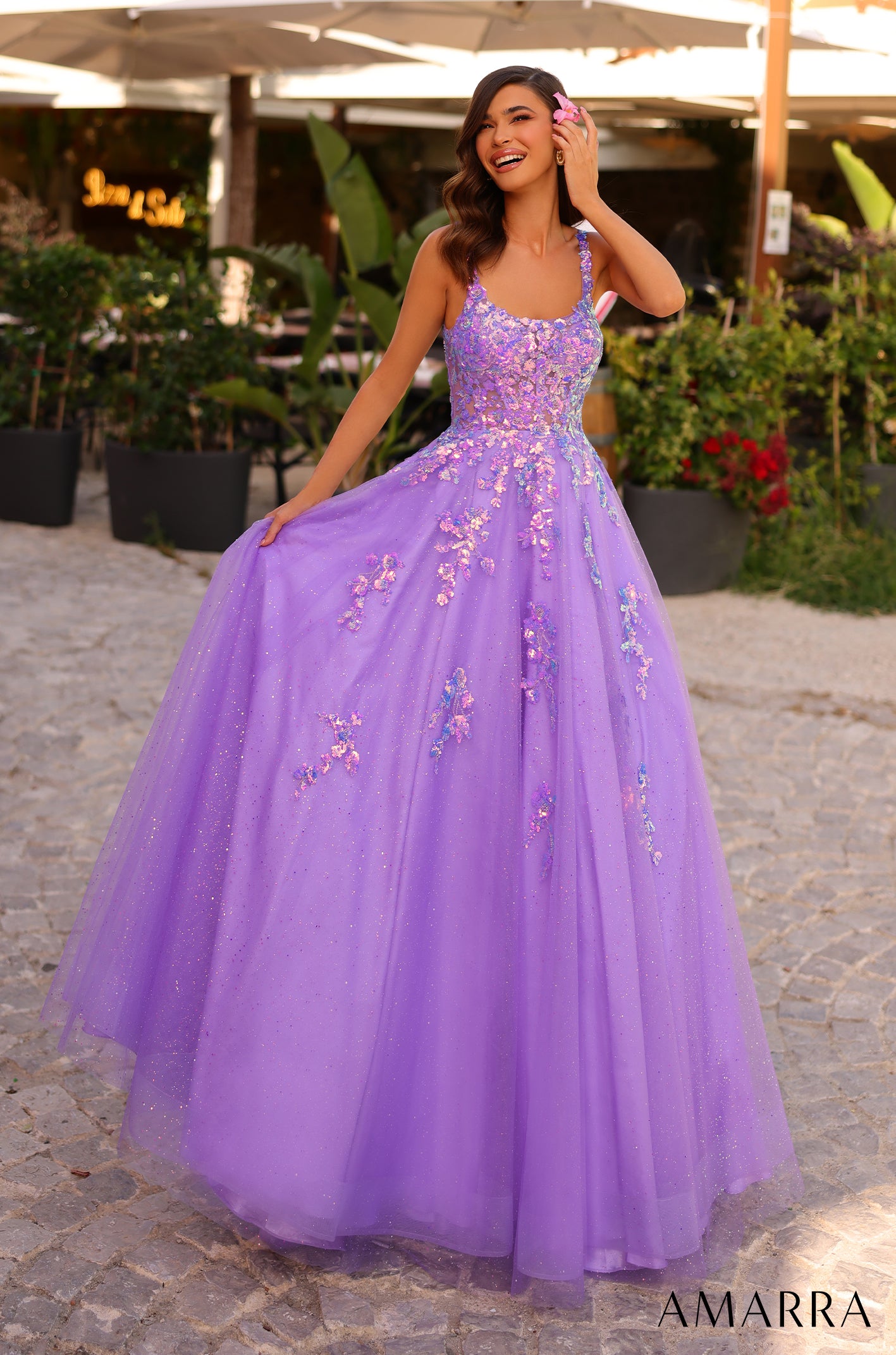 A woman in a lavender ballgown with floral embellishments smiles in a garden setting.