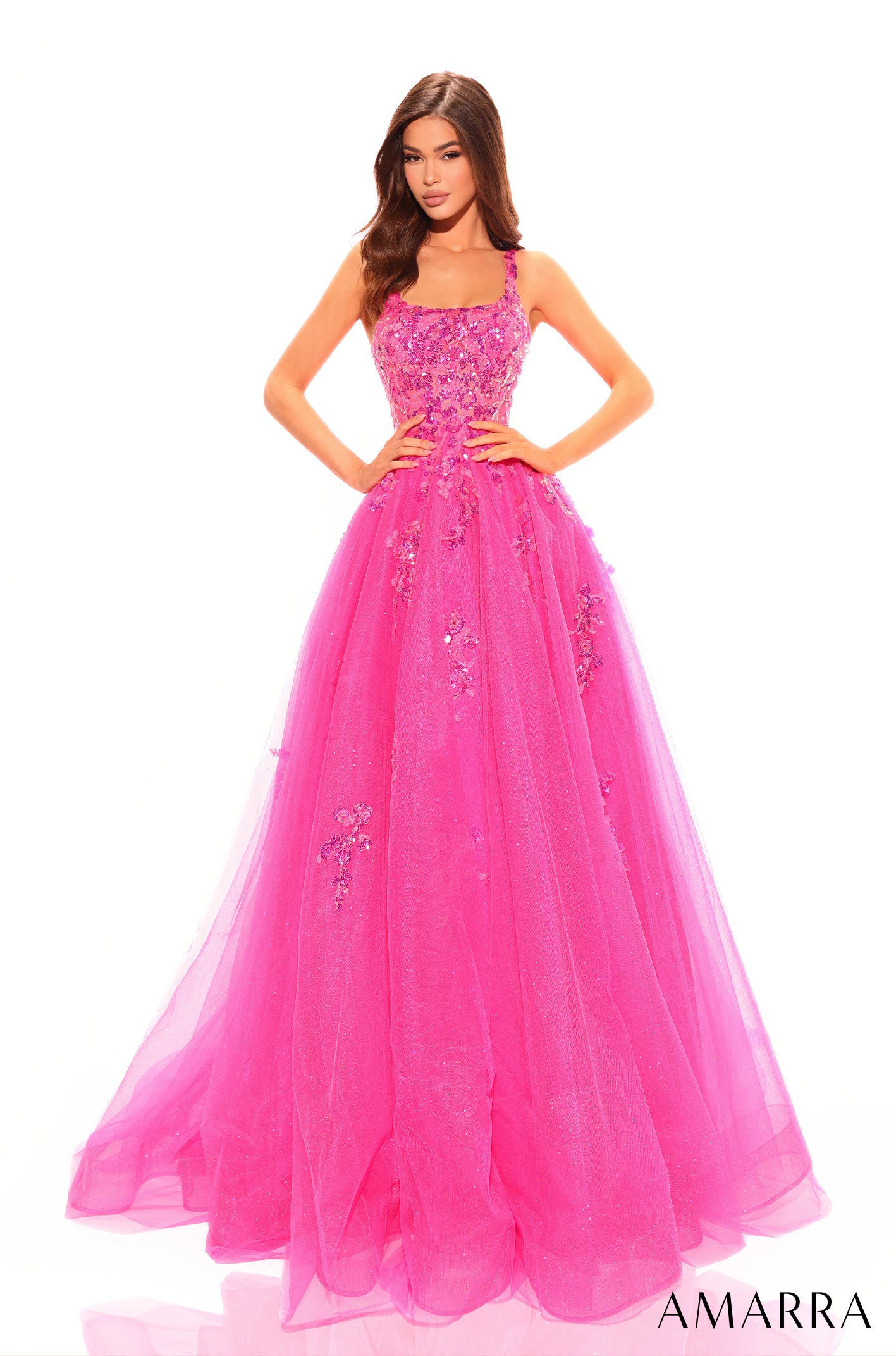 A woman wears a full-length fuchsia ball gown with floral appliqués and a fitted bodice by Amarra.