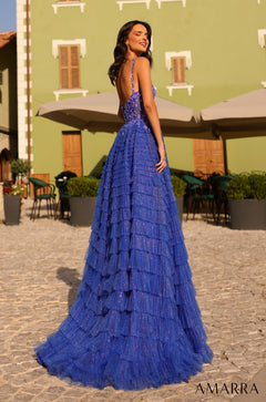 A long, tiered royal blue glittery gown with a fitted bodice, photographed in a sunlit courtyard with stone flooring.