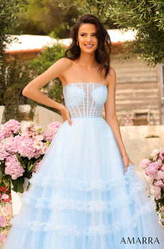 A woman in a light blue, strapless ball gown poses among pink flowers in an outdoor garden setting.