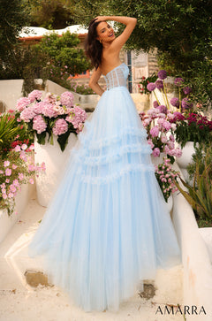 A woman in a light blue, tiered ball gown poses among pink and purple flowers in a garden setting.