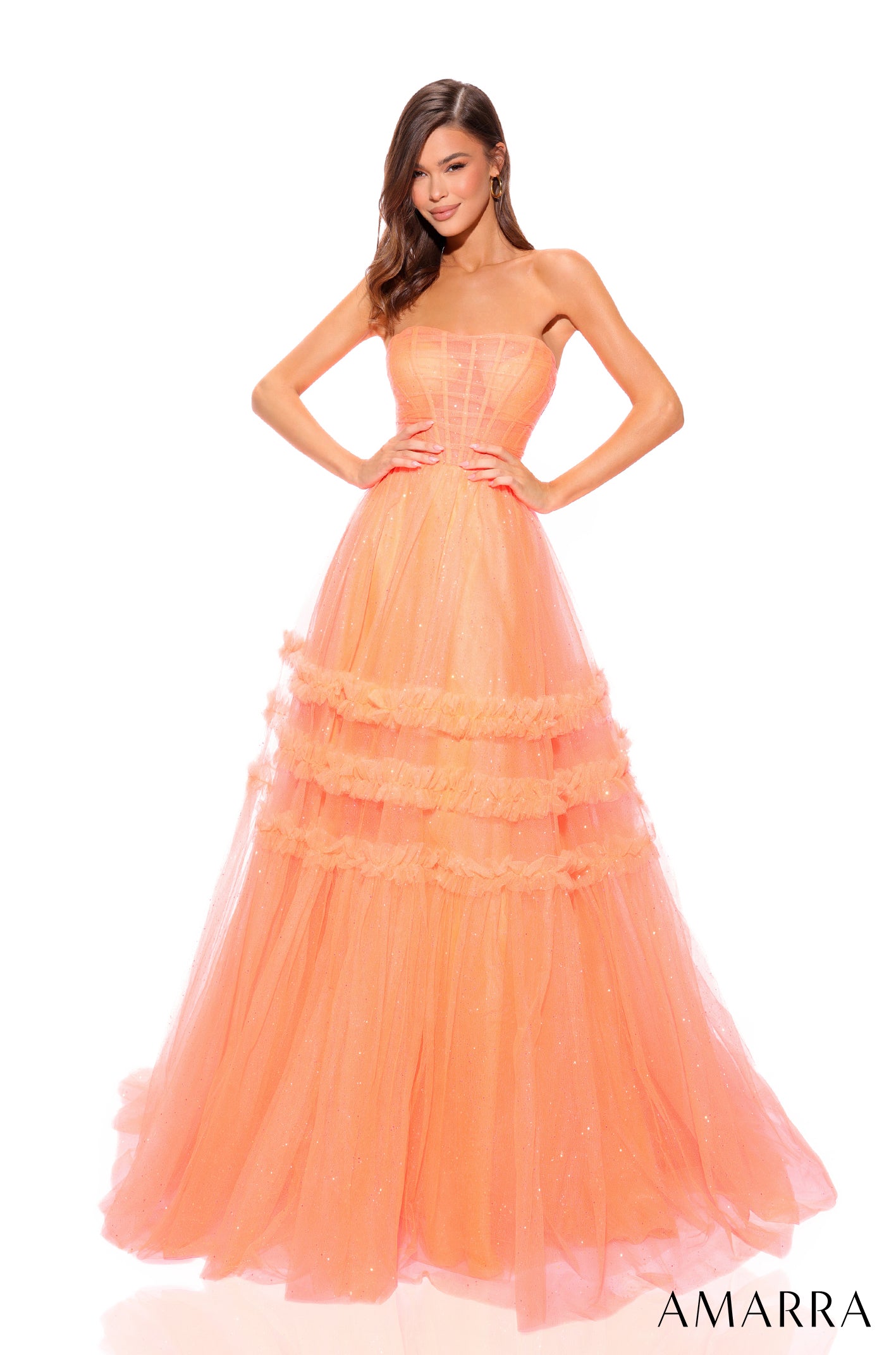 A model wears a full-length, tiered neon orange tulle gown with a strapless corset-style bodice.