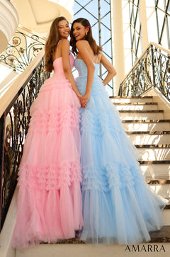 Two women in ruffled tulle gowns, one pink and one blue, stand together on an ornate staircase.