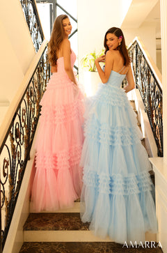 Two women in ruffled tulle gowns - pink and blue - pose on an ornate staircase with decorative wrought-iron railings.