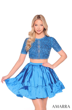 Model wears a peacock blue two-piece dress with a beaded crop top and tiered skirt, posing against a white background.