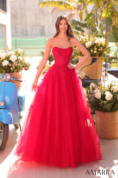 A woman wears a strapless, full-skirted Red ball gown with floral embellishments, standing near a blue scooter and flowers.