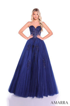 A woman wears a strapless navy blue ball gown with floral lace detailing and a full tulle skirt.