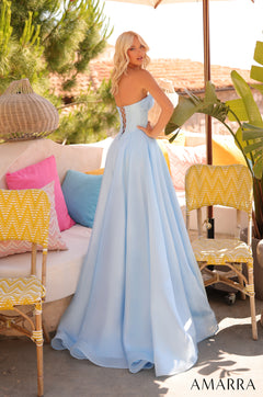 A woman in a light blue strapless ball gown poses on a patio with yellow and pink decor.