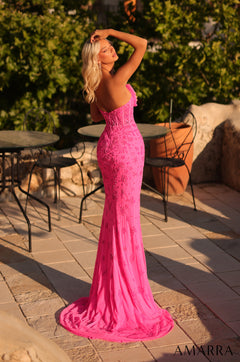 A blonde woman wears a vibrant pink mermaid-style lace gown on a stone patio at sunset.