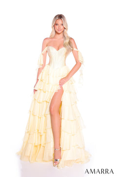 A model wears a flowing light yellow tiered gown with off-shoulder straps and a high leg slit.
