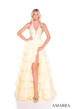 A woman wears a light yellow tiered halter gown with a plunging neckline and high leg slit, posing on a white background.
