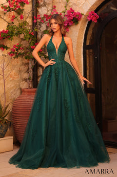 A woman wears an emerald green halter ball gown with lace details, standing before a stone wall with pink flowers.