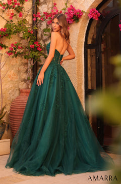 A model wears an emerald green lace ball gown, standing before a stone wall with pink bougainvillea flowers.