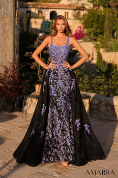 A woman wears a Black/Multi floral-embroidered gown with a long train in an outdoor garden setting.