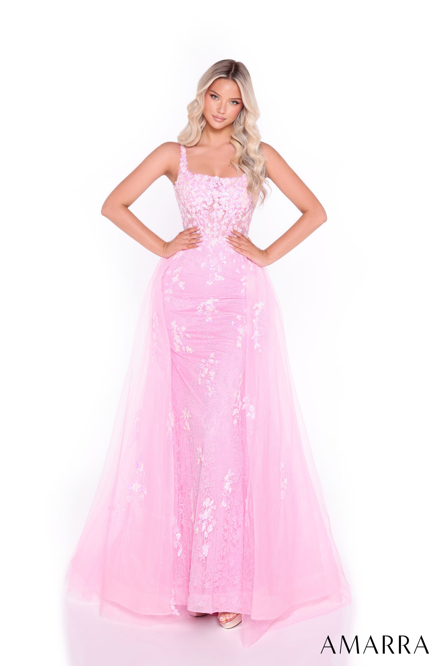 A model wears a fitted Light Pink sequin gown with a flowing tulle overskirt and square neckline.