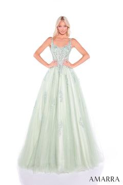 A woman wears a sage green ball gown with an embellished corset bodice and flowing tulle skirt by Amarra.