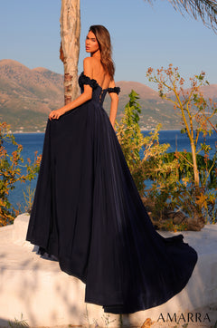 A person in a navy off-shoulder ball gown stands by a tree with mountains and blue water in the background.