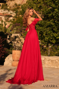 A woman wears a flowing red evening gown with lace details, posing in a garden with stone walls.