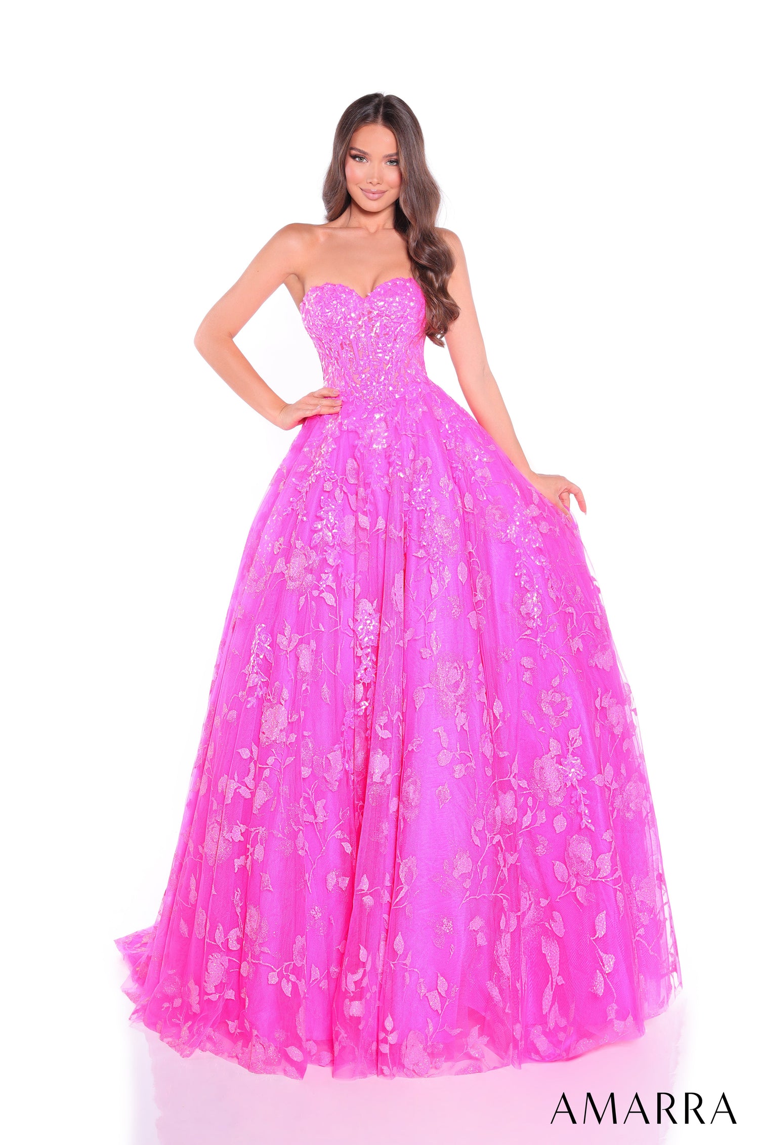 A model wears a strapless fuchsia ballgown with floral embellishments and a sweetheart neckline.