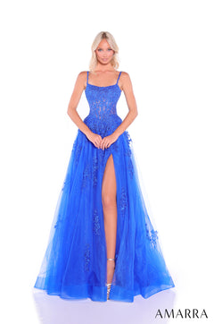 A model wears a Royal Blue corseted gown with lace details and a high slit, standing against a white backdrop.