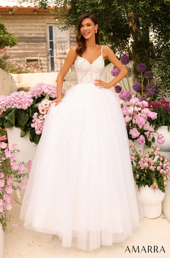 A woman in a white beaded ballgown poses among pink and purple flowers, wearing spaghetti strap wedding dress by Amarra.