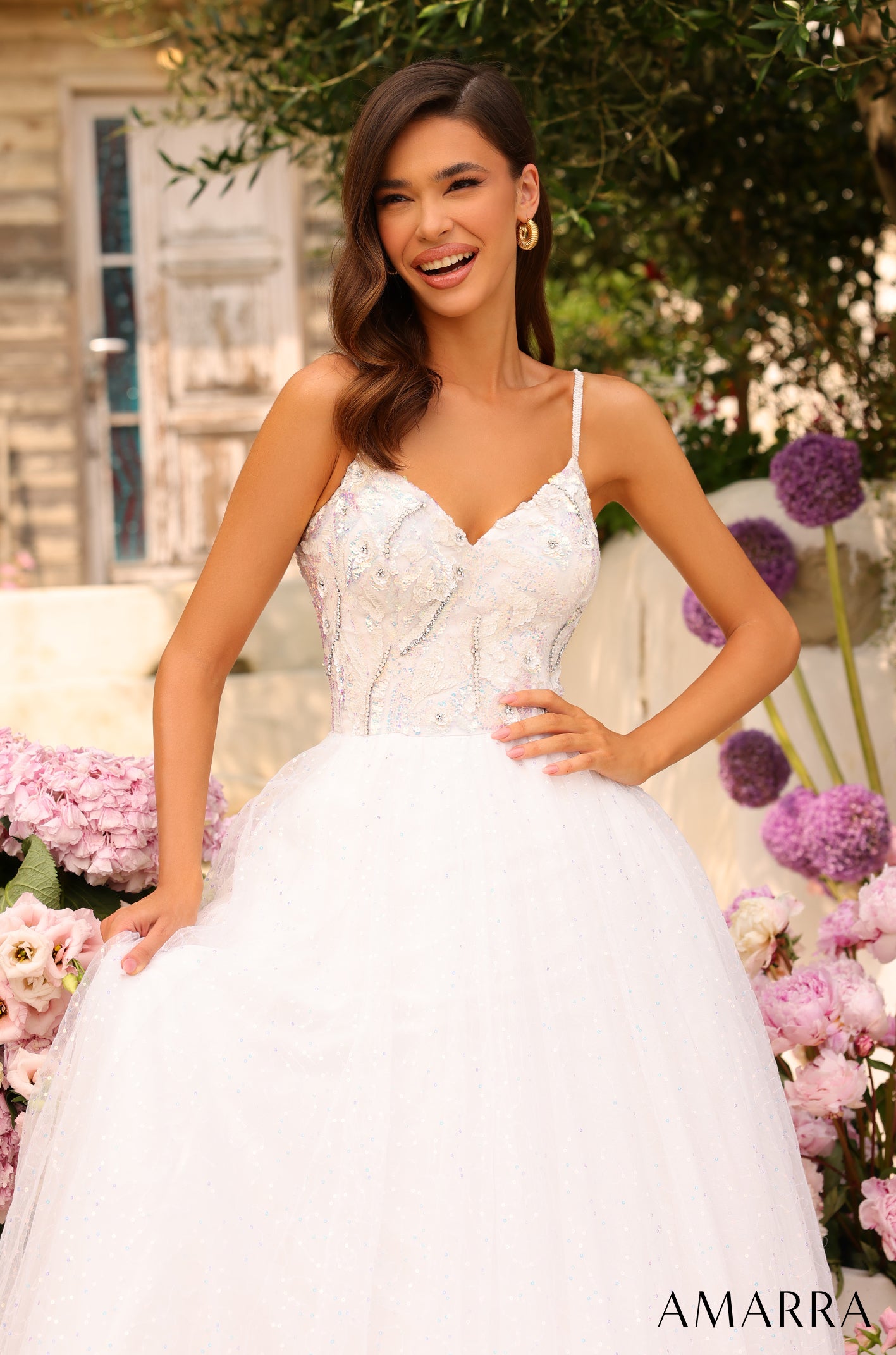 A bride in a white embellished ball gown smiles, surrounded by pink and purple flowers.