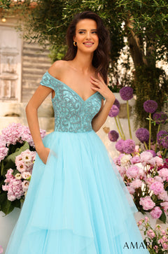 A smiling woman wears a teal off-shoulder ballgown with beaded bodice among pink and purple flowers.