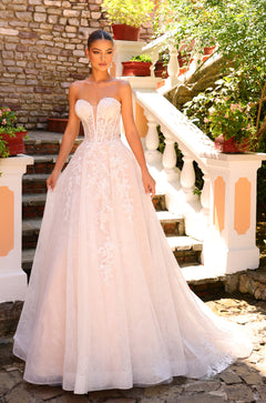 A model wears a blush strapless ballgown wedding dress with lace details on a stone staircase.