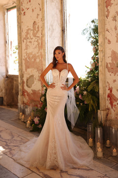 Bride in a strapless lace mermaid wedding gown stands amid candles and flowers in a distressed room.