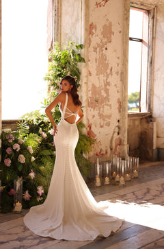 A bride in a white mermaid-cut wedding dress poses in a rustic room with candles and greenery.