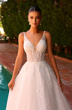 Model in shimmering white wedding gown with deep V-neckline stands poolside in elegant pose.