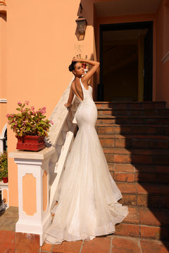 A bride in a white mermaid-style wedding gown with a long train poses elegantly on terracotta steps.