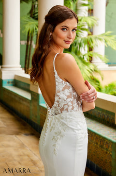 A woman in a white lace wedding dress poses elegantly beside white columns with tropical greenery.
