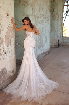 A strapless mermaid wedding gown with delicate lace overlay and flowing tulle train in a distressed room.