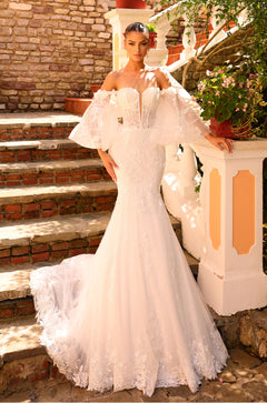 A model wears an off-shoulder white lace mermaid wedding dress with billowing sleeves on brick steps.