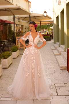 A model wears a blush A-line wedding dress with delicate lace appliqués in a charming European street setting.