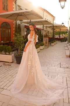 A bride in a delicate lace wedding gown stands on a charming European street with a long, flowing train.
