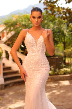 A woman wears an elegant blush lace mermaid wedding dress with delicate floral embroidery in an outdoor garden setting.